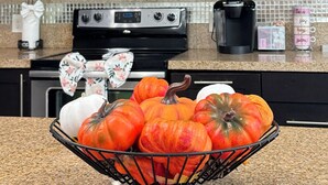 A kitchen with dark cabinets, a stainless steel microwave, a stove, and a bowl of pumpkins on the counter. - Fully Furnished 3BR/2BA Condo with Balcony. Close to Airport, Shopping & Dinning (McAllen)