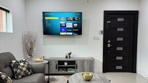 Un salon moderne avec un canapé gris, une table basse, un téléviseur fixé au mur et un ventilateur de plafond.