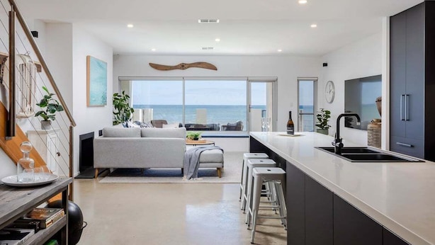 Ett modernt kök med en stor köksö, en matplats med utsikt över havet och ett vardagsrum med en soffa och ett soffbord.