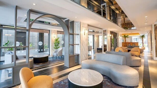 Un hall d’hôtel moderne, doté d’espaces aménagés avec des sièges, de grandes fenêtres et un plafond haut.