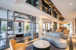 Un hall d’hôtel moderne, doté d’espaces aménagés avec des sièges, de grandes fenêtres et un plafond haut.
