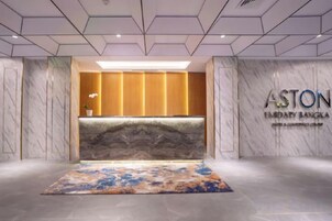 Un área de recepción con un mostrador de mármol, un tapete grande y una pared con el letrero 'ASTON Limadia Bangkok'.