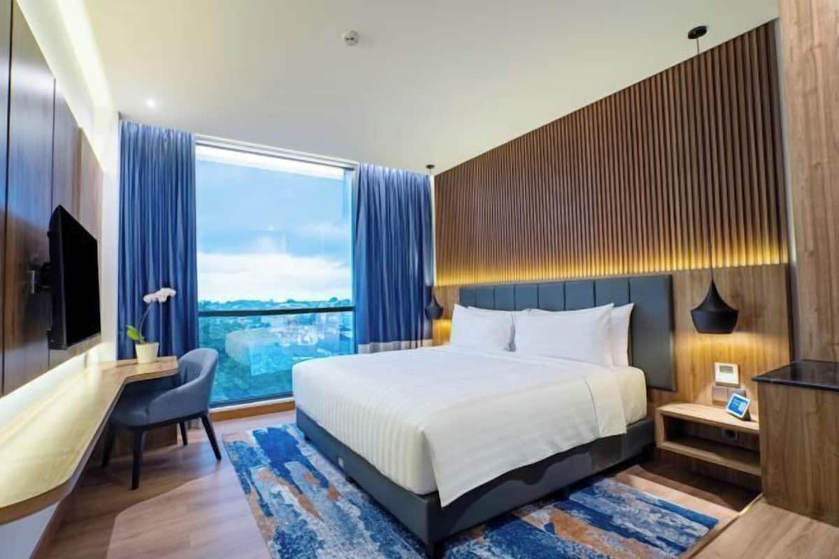 Una habitació d'hotel moderna amb un llit gran, un escriptori i vistes a la ciutat.