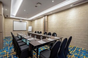 Una sala de conferencias con una larga mesa, sillas, una pantalla de proyector y una pizarra.
