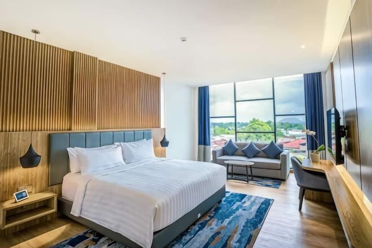 Habitació d'hotel moderna amb un llit gran, un sofà, una taula petita i un televisor.