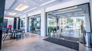 Un hall d’hôtel moderne avec des portes vitrées, un espace détente avec des tables et des chaises, et un comptoir d’accueil.