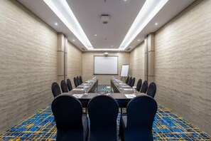 Un salón de conferencias con una mesa larga, sillas, una pantalla de proyector y una pantalla de presentación.