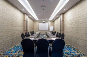 Un salón de conferencias con una mesa larga, sillas, una pantalla de proyector y una pantalla de presentación.