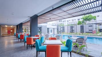 A modern outdoor seating area with tables and chairs, a pool, and a view of the surrounding buildings.