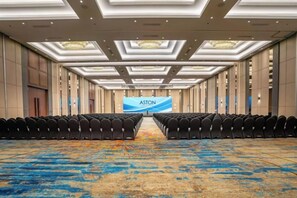 A conference room with rows of chairs, a large screen displaying 'ASTON,' and a patterned carpet.
