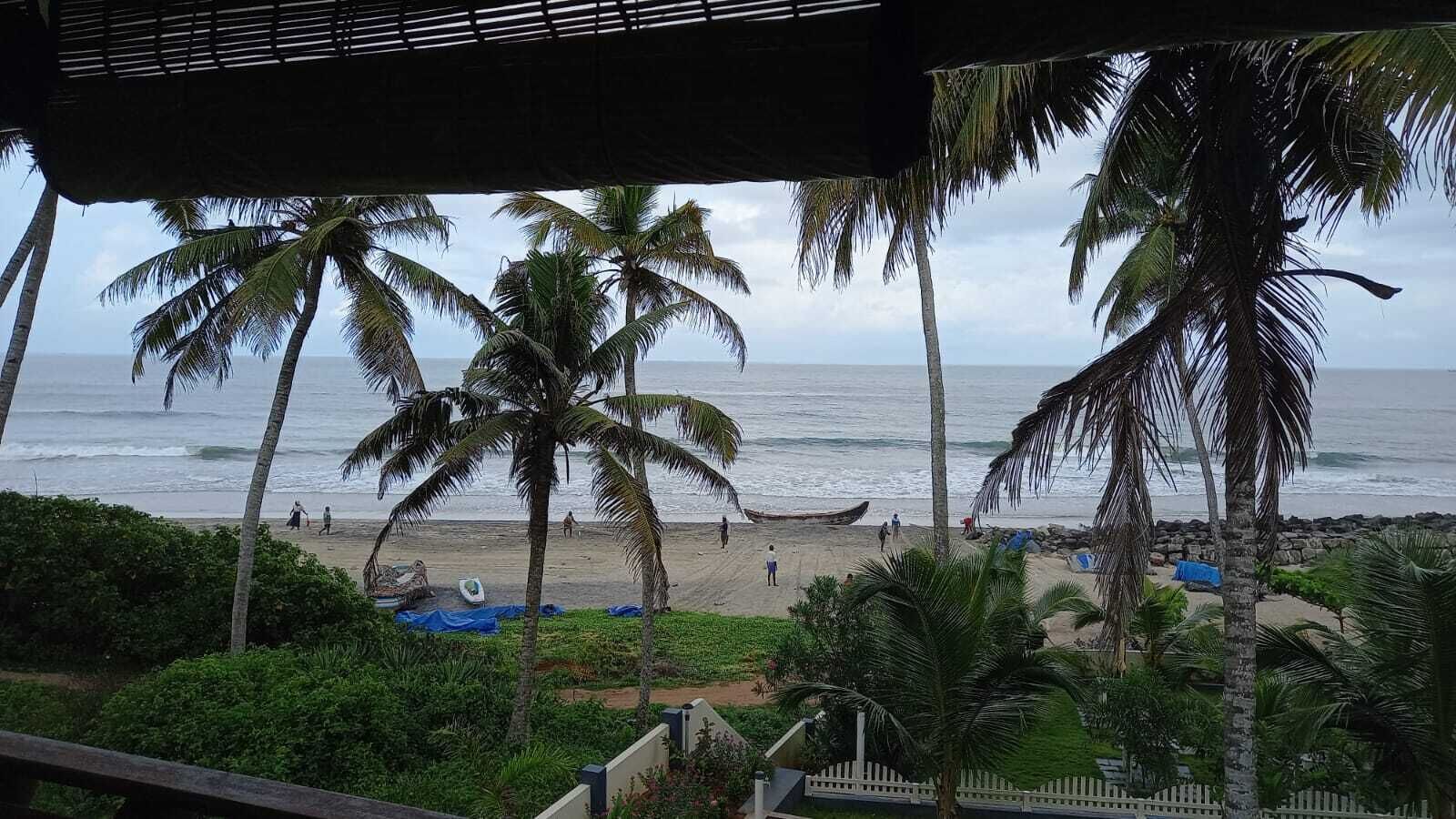 Blick auf einen Strand mit Palmen, ein Boot im Sand und eine Holzlattenveranda.