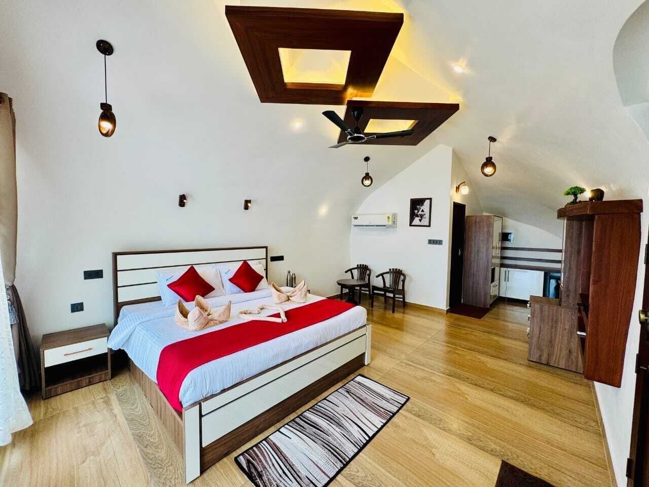 Een moderne slaapkamer met een groot bed, een plafondventilator en een kleine kitchenette op de achtergrond.