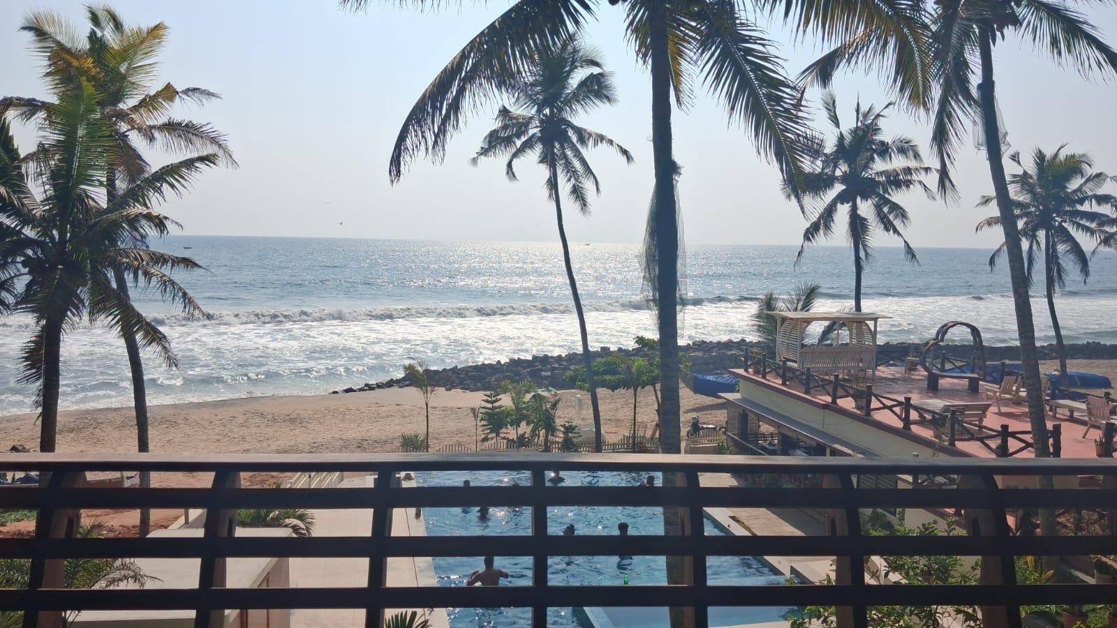 A beach view with palm trees, a pool, and a wooden deck with lounge chairs.