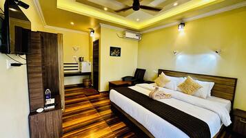 A hotel room with a large bed, wooden flooring, a ceiling fan, and a TV mounted on the wall.