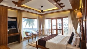 A spacious bedroom with a large bed, wooden ceiling beams, a balcony with chairs, and a TV. - Maadathil cottages & Beach resort (Varkala)
