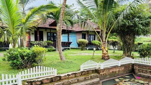 A traditional house with a tiled roof, surrounded by lush greenery and a small pond with lily pads and pink flowers. - Maadathil cottages & Beach resort (Varkala)