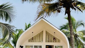 A small, single-story building with a triangular roof, surrounded by palm trees. - Maadathil cottages & Beach resort (Varkala)
