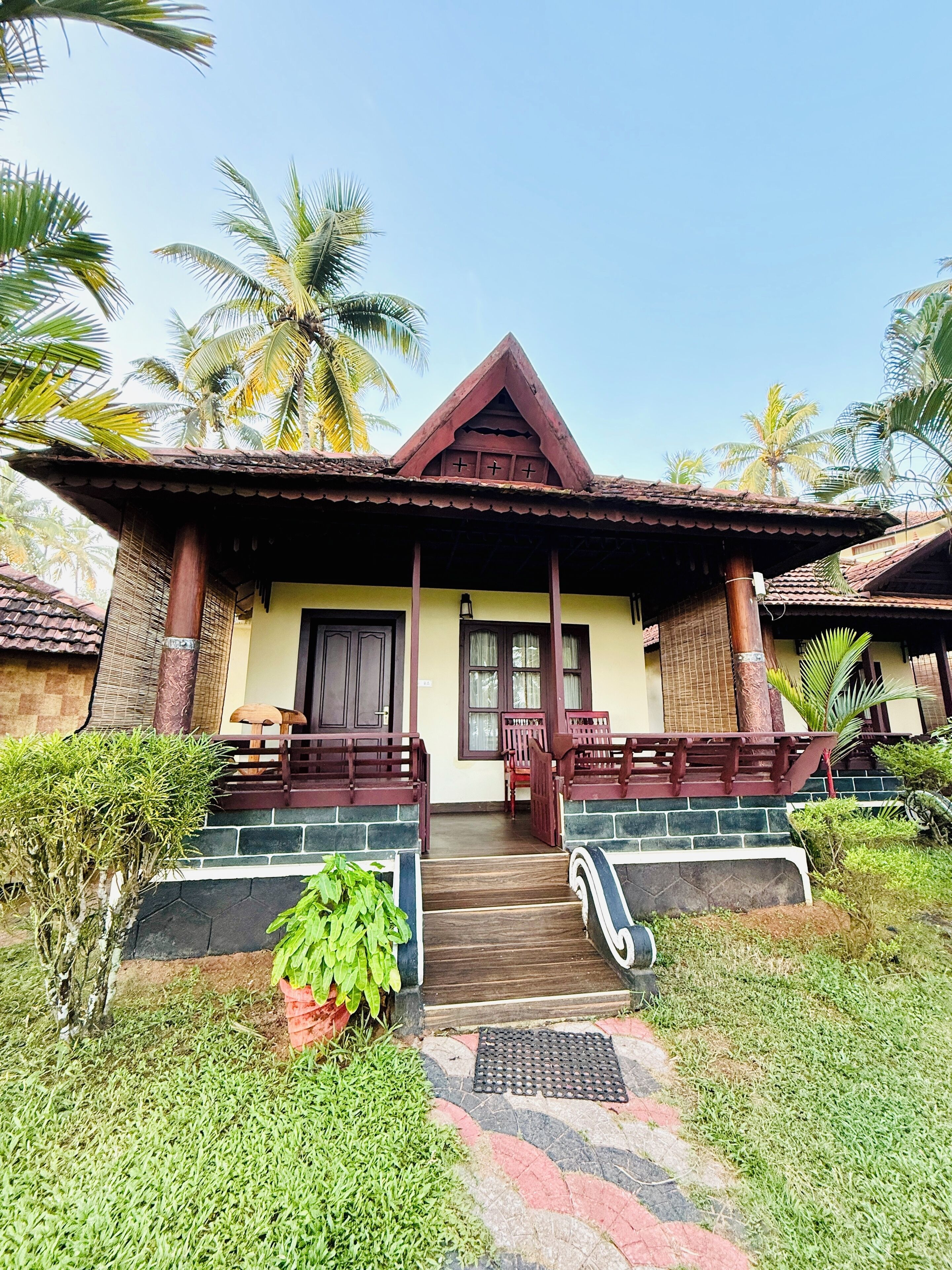 A bungalow with a tiled roof, a porch with wooden railings, and a small garden area with potted plants.