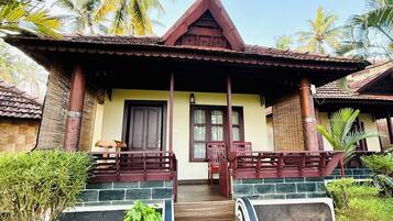 A bungalow with a tiled roof, a porch with wooden railings, and a small garden area with potted plants.