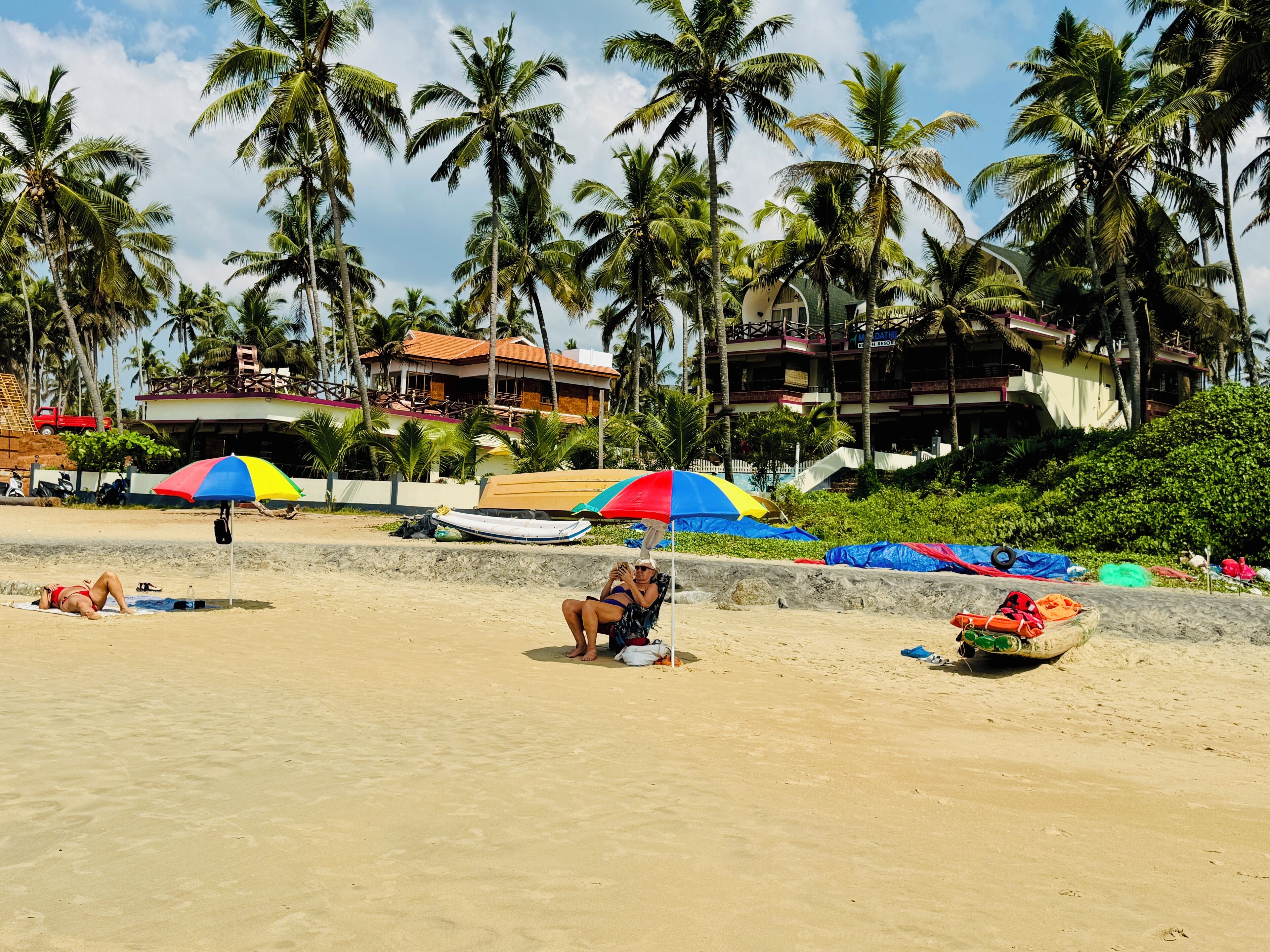 A beach with palm trees, a sandy shore, and a building with a red roof in the background.