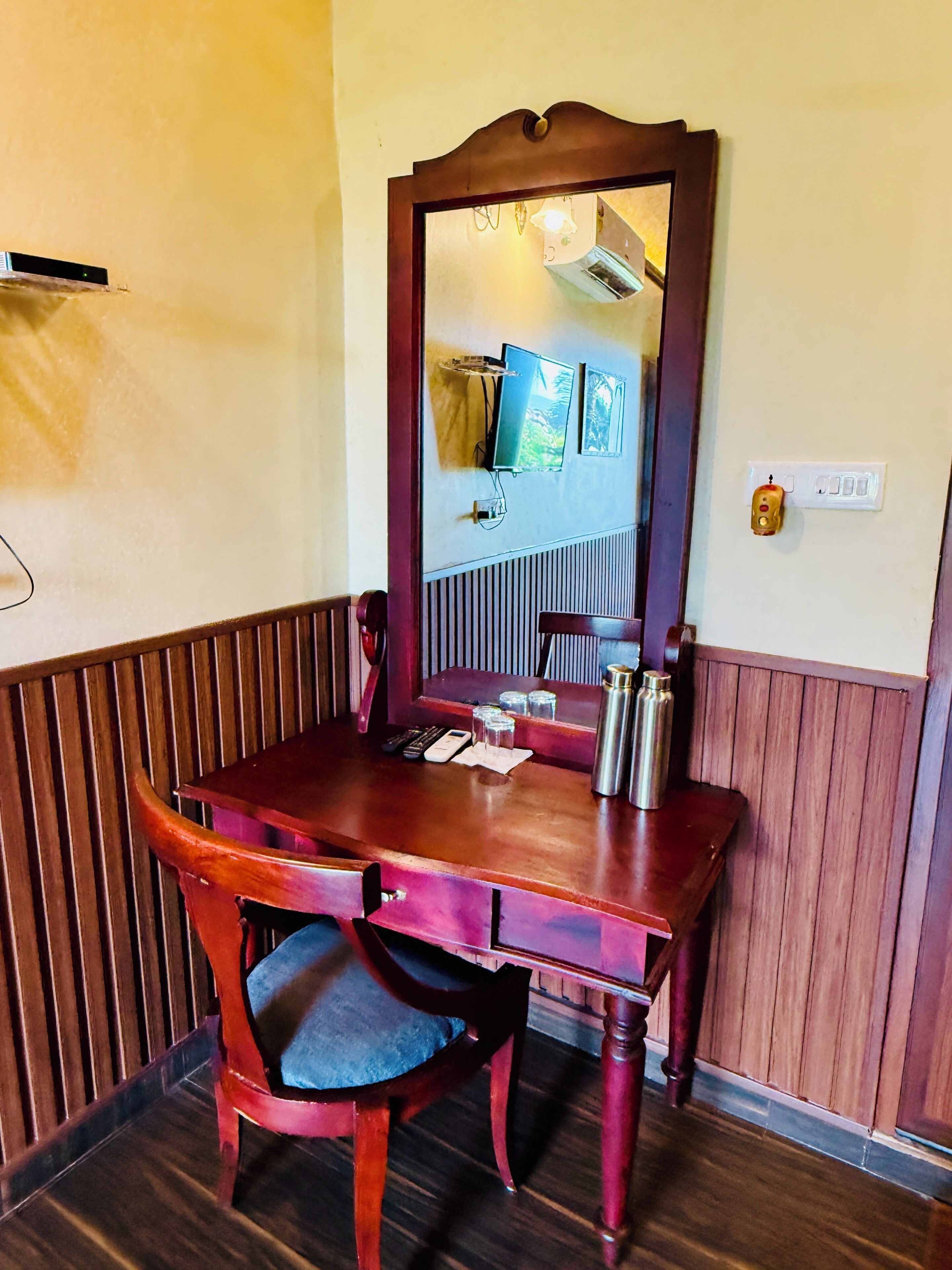 A wooden desk with a mirror, a chair, and a small table with a thermos.