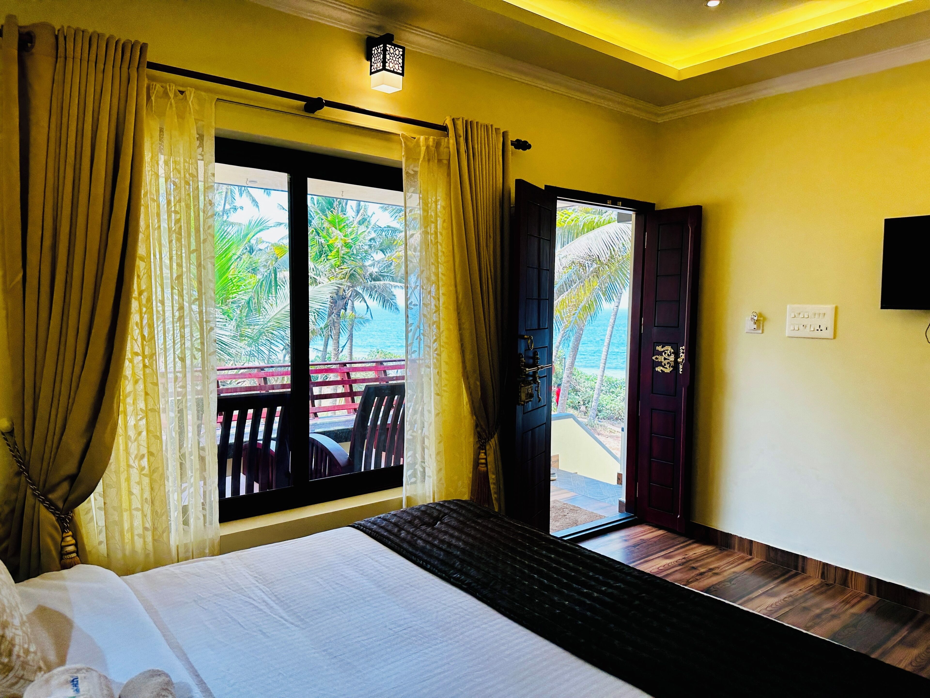 A hotel room with a bed, a view of the ocean, and a balcony with chairs.