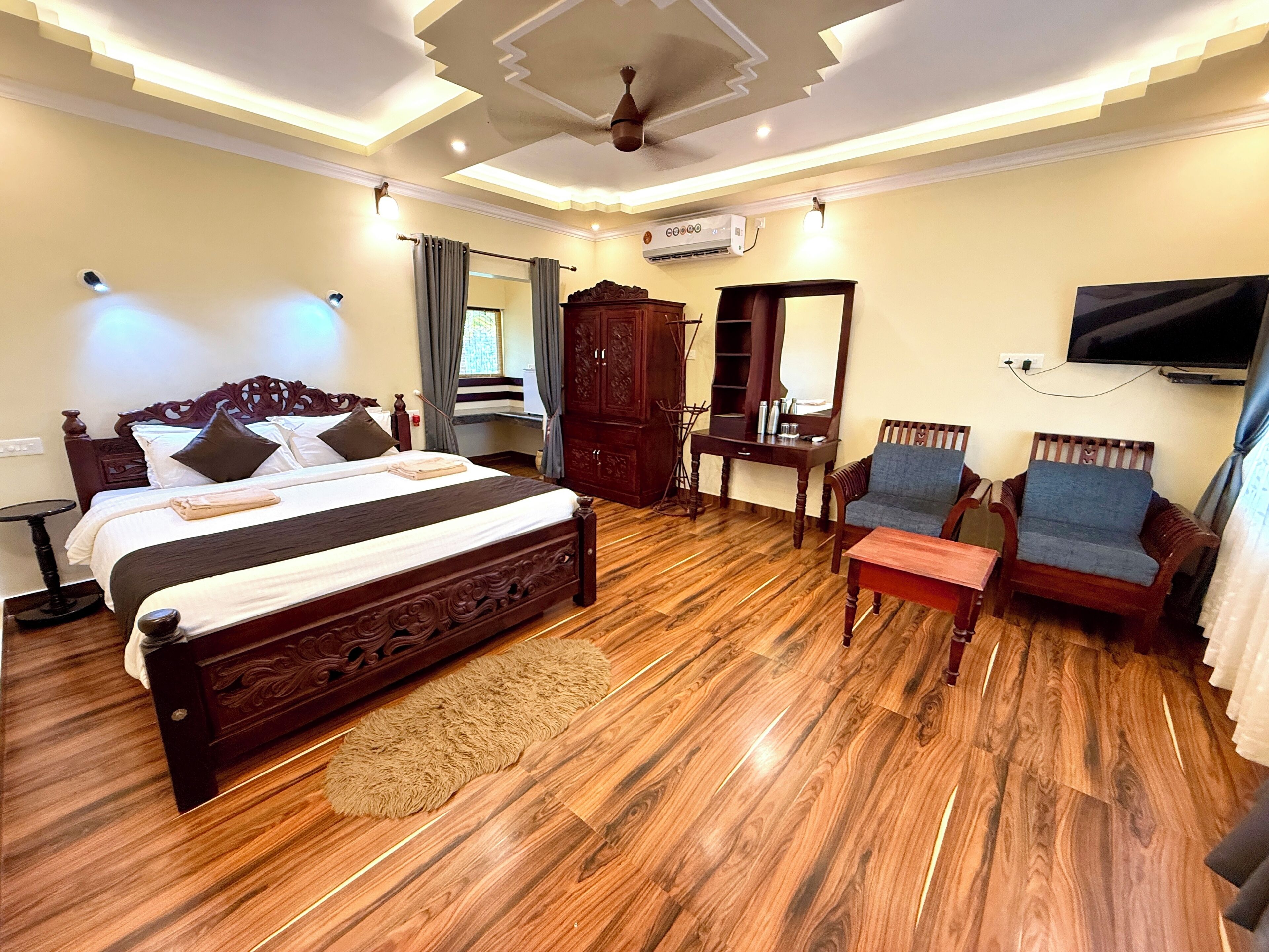 A hotel room with a large bed, wooden furniture, a television, and an air conditioning unit.