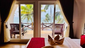 A room with a bed, a red throw blanket, and a view of the beach and palm trees through a glass door. - Maadathil cottages & Beach resort (Varkala)