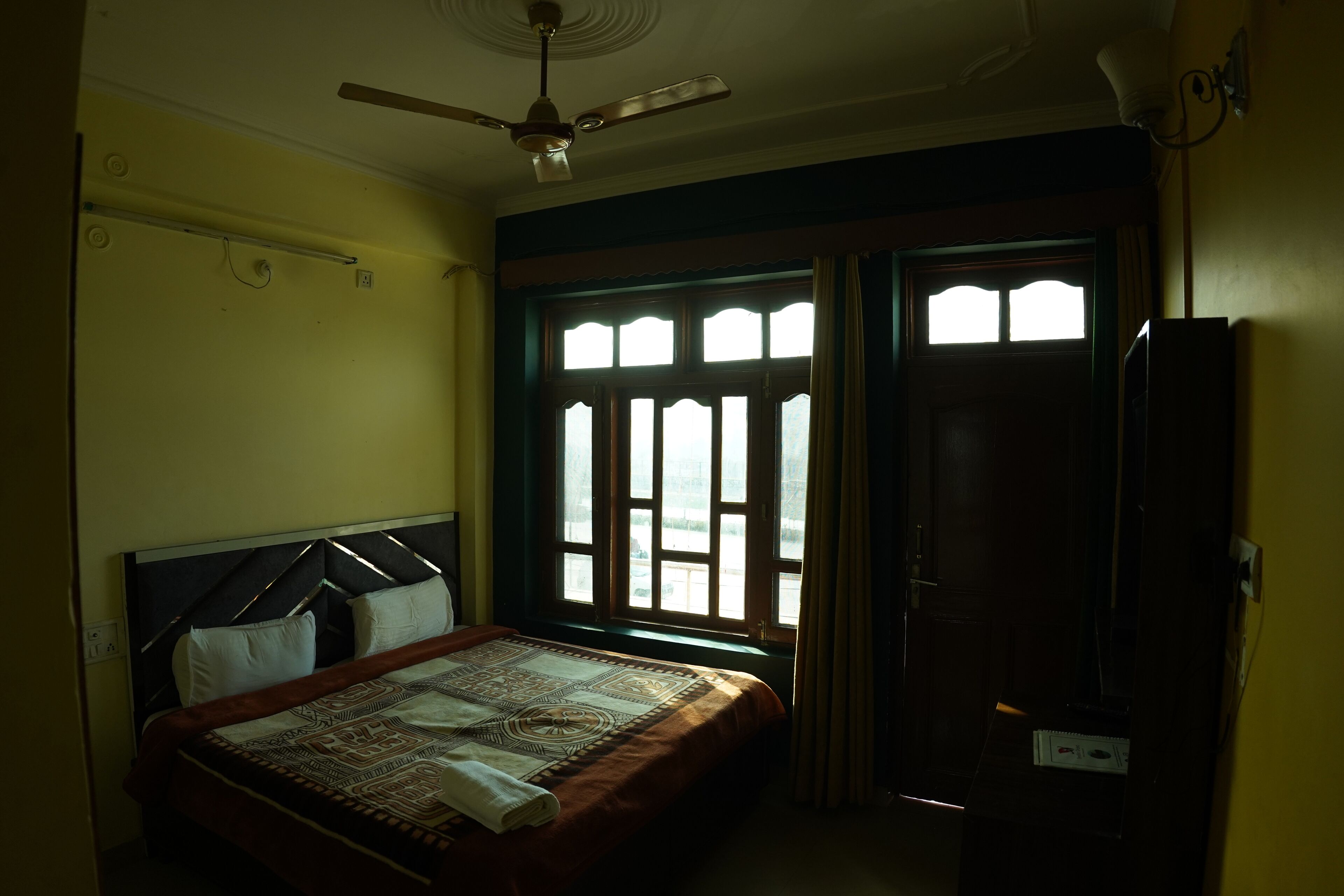 A bedroom with a bed, a ceiling fan, a window with curtains, and a door.