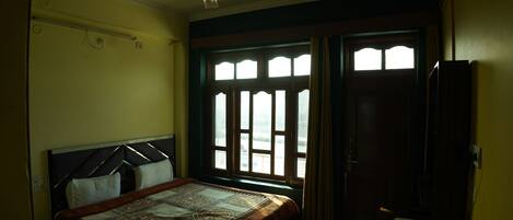 A bedroom with a bed, a ceiling fan, a window with curtains, and a door.
