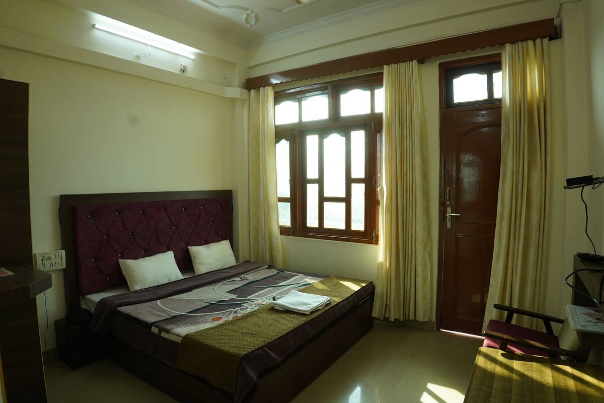 A neatly arranged bedroom with a large bed, a bedside table, a desk, and a window with curtains.