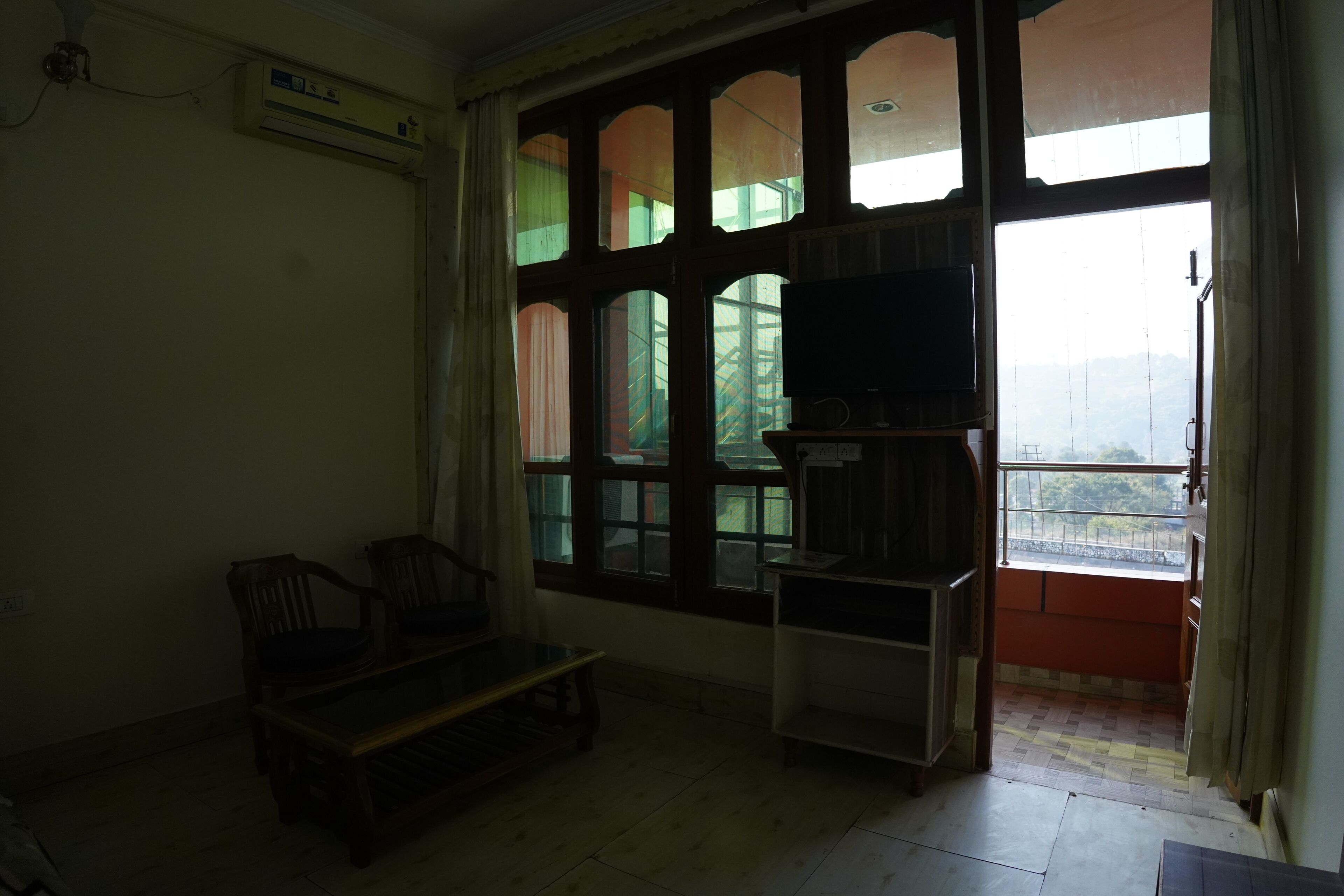 A room with a large window, a television on a stand, and two chairs.