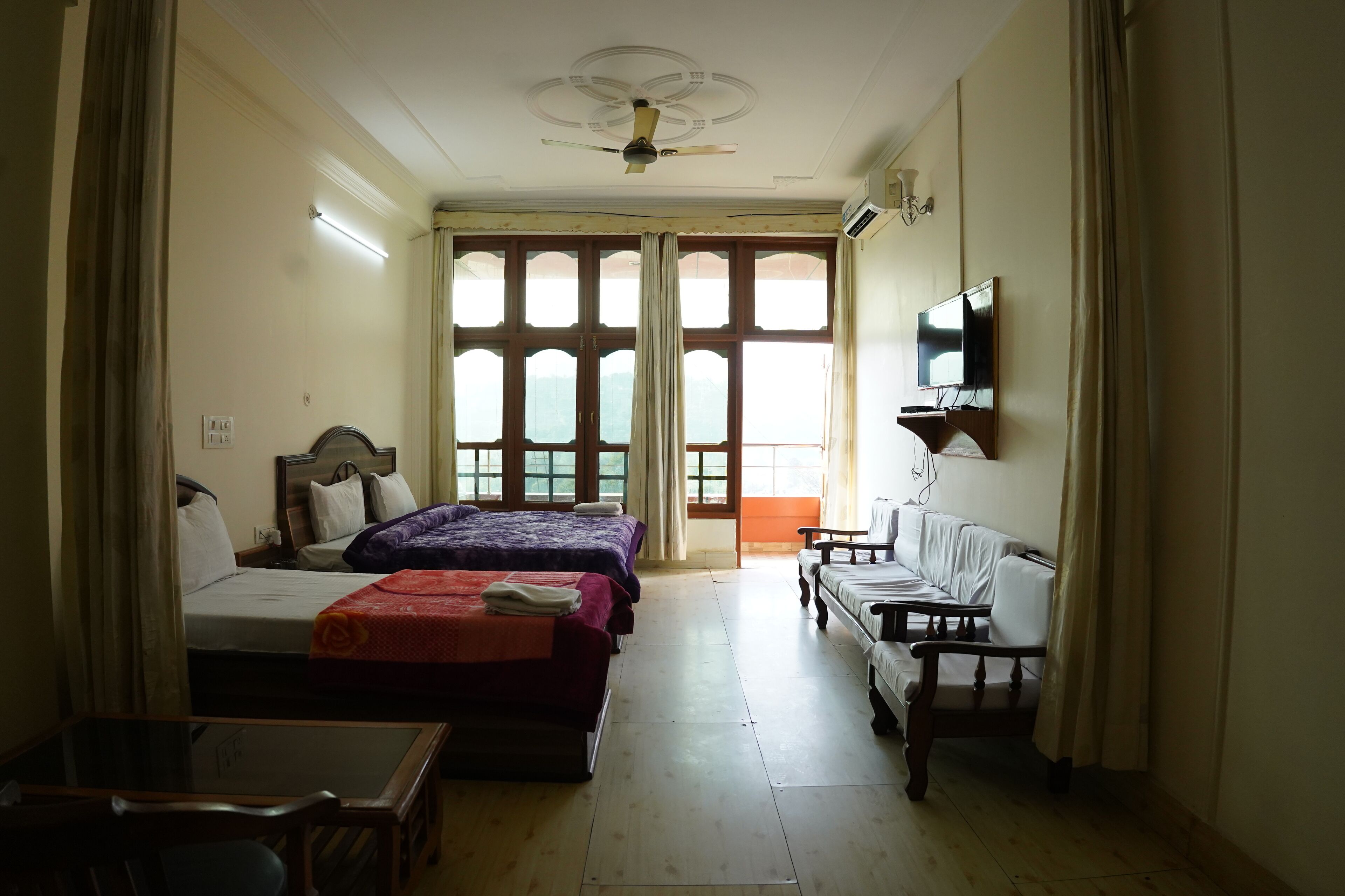 Habitación de hotel con dos camas, un sofá, un televisor y ventanas amplias.