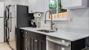 A modern kitchen with a stainless steel refrigerator, a built-in dishwasher, a double sink, and white cabinetry. - Charming 2-bedroom house in welcoming University Place with AC (University Place)