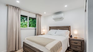 A bedroom with a wooden bed, two bedside tables with lamps, a window with curtains, and an air conditioning unit. - Charming 2-bedroom house in welcoming University Place with AC (University Place)