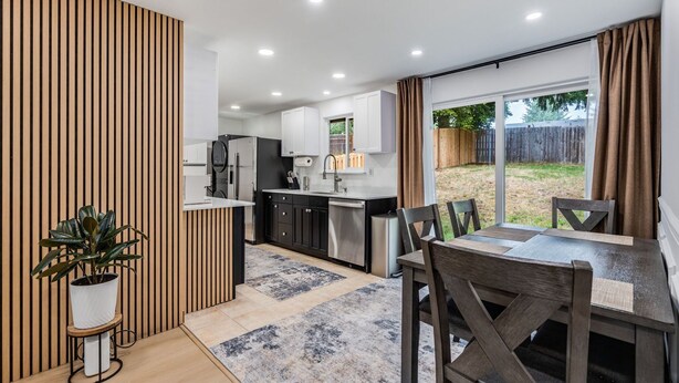 A modern kitchen with a dining area, wooden paneling, and a view of the backyard. - Charming 2-bedroom house in welcoming University Place with AC (University Place)