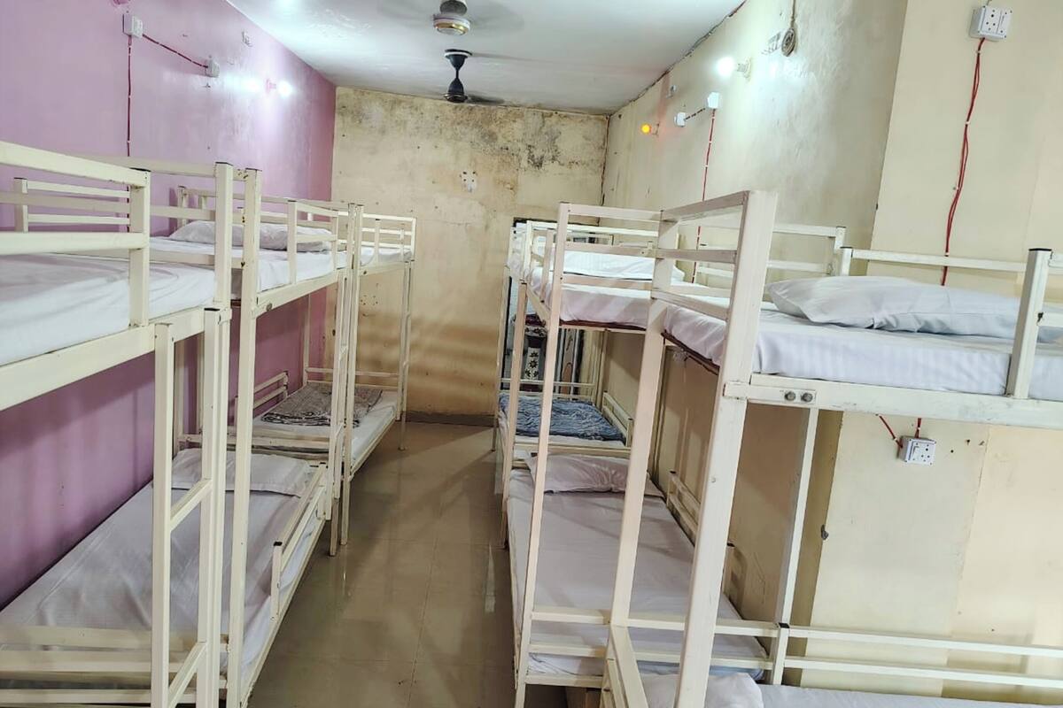 Une chambre de dortoir avec des lits superposés, un ventilateur de plafond et une prise électrique au mur.