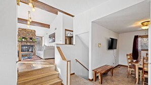 A modern interior with a wooden staircase, a stone fireplace, a dining area with wooden furniture, and a flat-screen TV mounted on the wall. - Lead Haven Lodge: Mountain Retreat w/ Hot tub (Lead)
