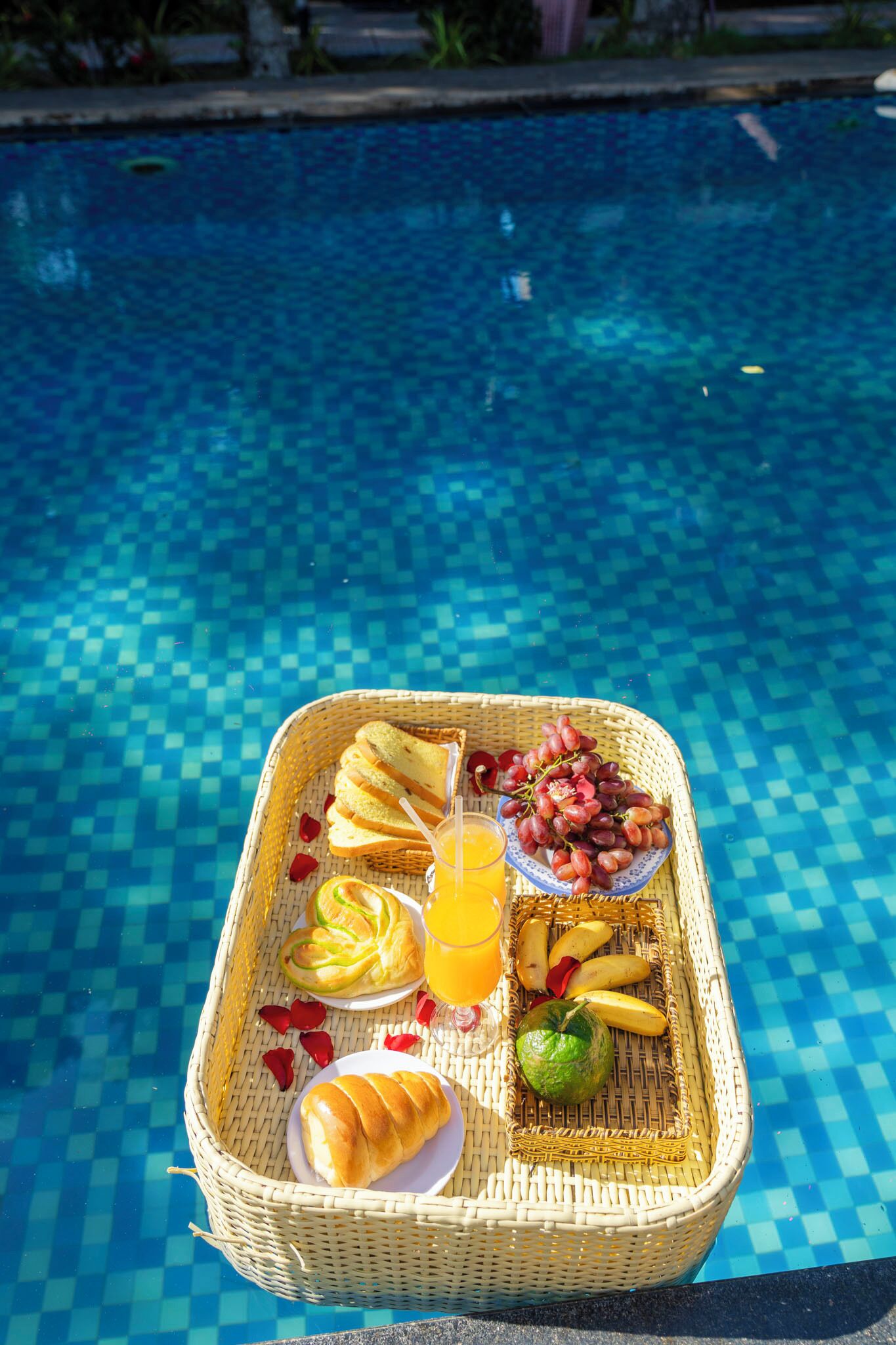 A wicker tray with food and drinks by a pool.