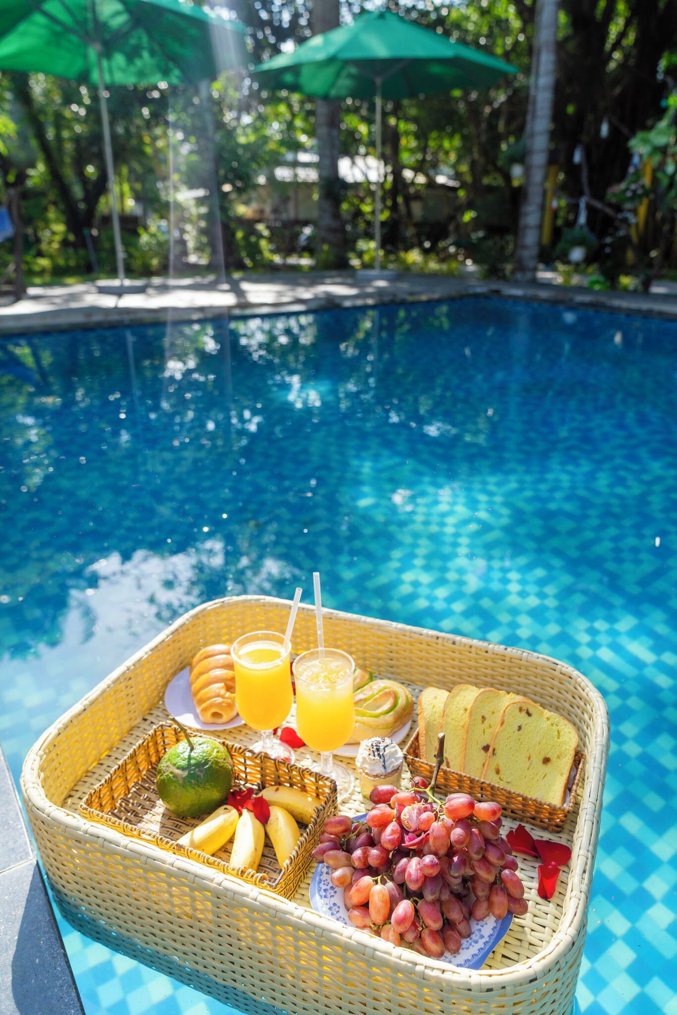Colazione a bordo piscina, con un cesto in vimini pieno di frutta, pane e bevande.