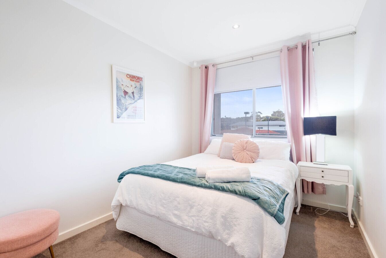 Een slaapkamer met een groot bed, een nachtkastje, een lamp en een raam met gordijnen.
