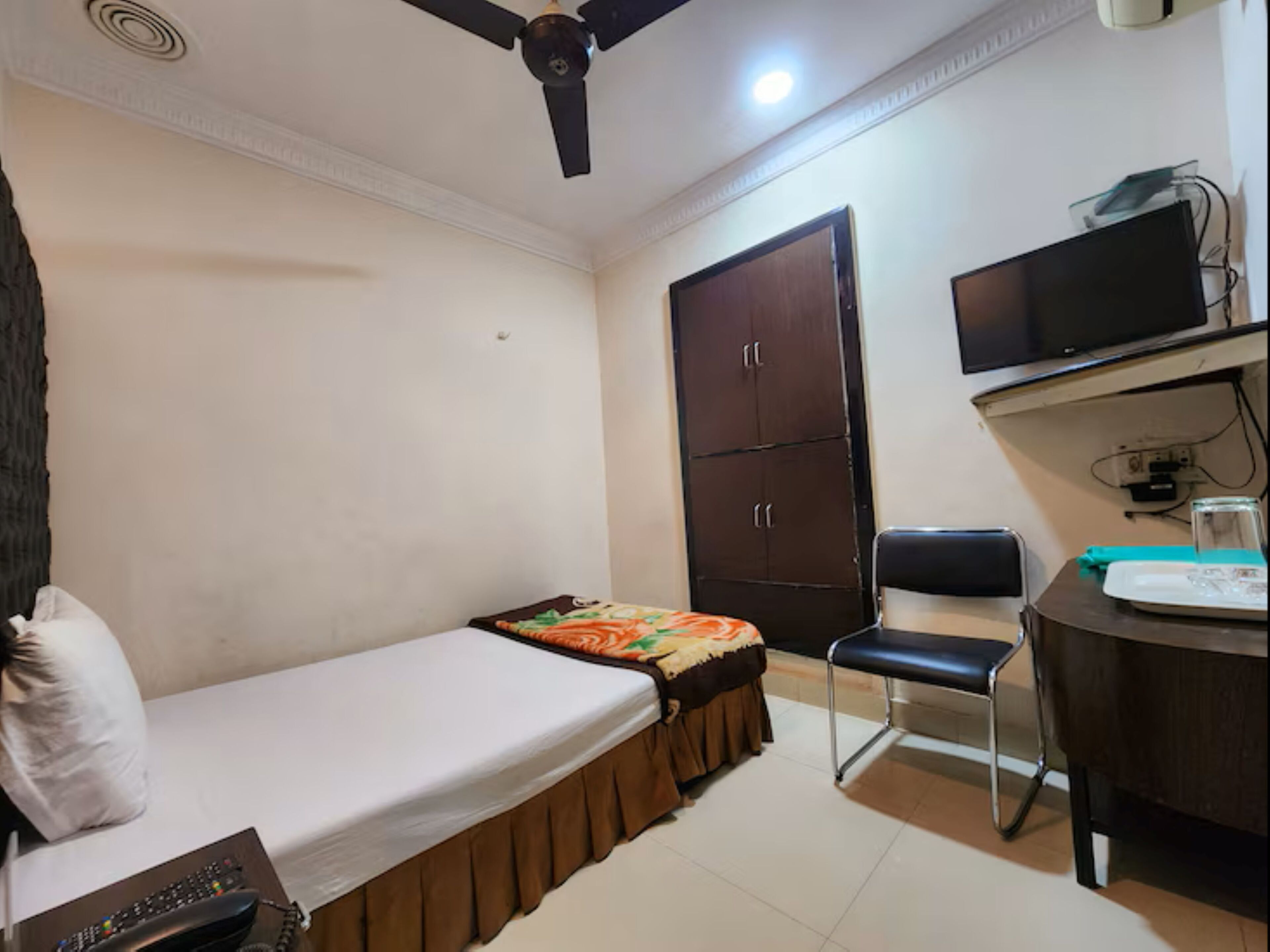 A small bedroom with a single bed, a desk with a chair, a wardrobe, and a ceiling fan.