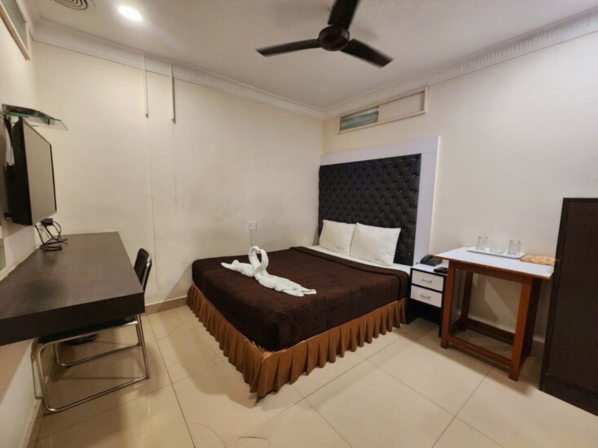 Habitación de hotel con cama, escritorio, silla, mesita de noche y ventilador de techo.