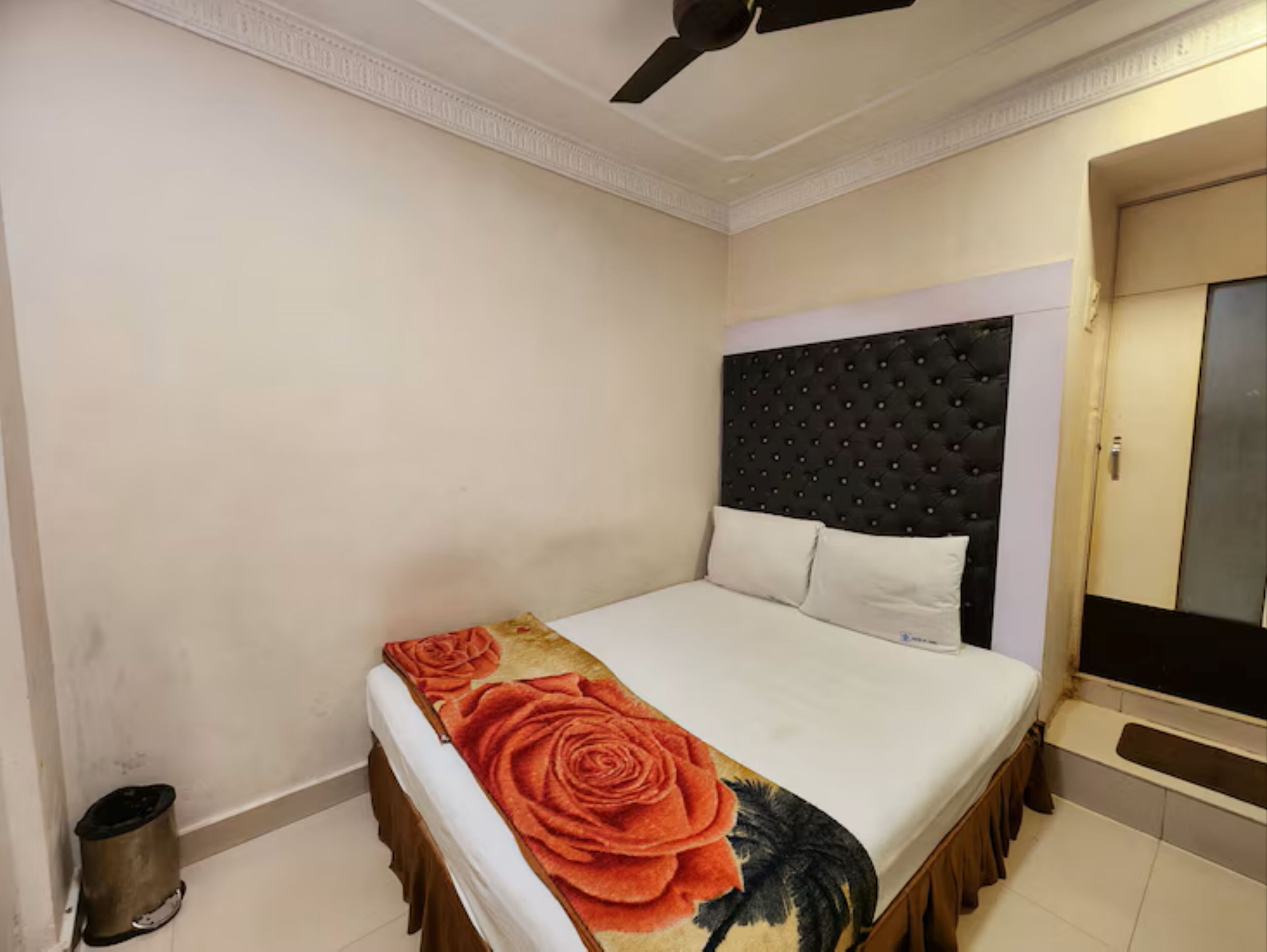 A bedroom with a bed, a ceiling fan, a door, and a trash bin.