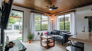 Un soggiorno moderno con soffitto in legno, una ventola a soffitto, un divano, un tavolino da caffè e una televisione.