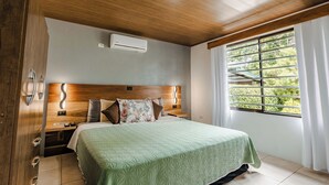 Una camera da letto con soffitto in legno, un letto grande con copripiumino verde, un comodino e una finestra con tende.