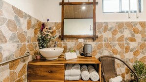 Un bagno con parete in pietra, mobile lavabo in legno, un lavandino ampio, un portascopevoli e uno specchio.