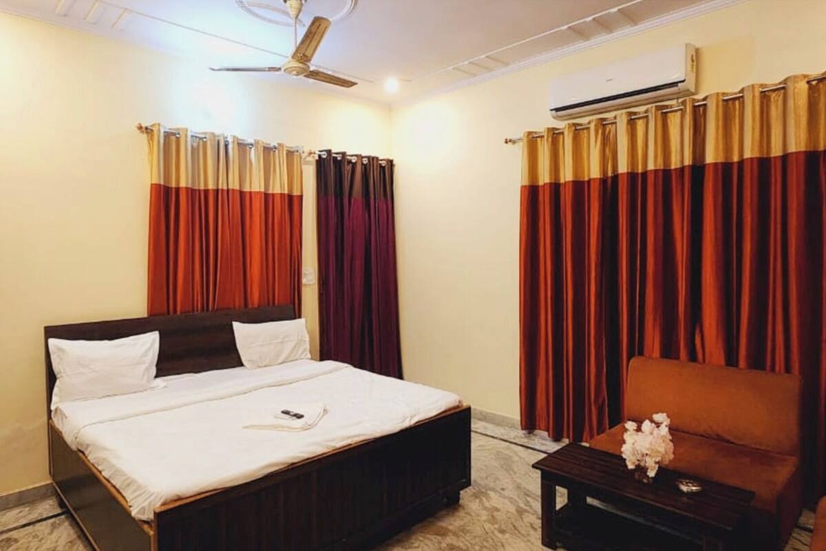 Una habitación de hotel con cama, mesita de noche, sofá, cortinas, equipo de aire acondicionado y ventilador de techo.