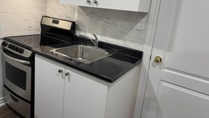 A kitchen with white cabinets, a black countertop, stainless steel sink, and a built-in oven. - Cozy, Private Suite, Two Level Apartment With Separate Entrance (Brampton)