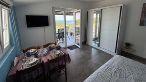 Una stanza con un tavolo da pranzo per quattro persone, una TV montata a parete e una porta scorrevole che dà su un balcone con vista.